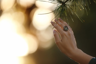Young woman wearing beautiful silver ring with prehnite gemstone near pine, closeup. Space for text