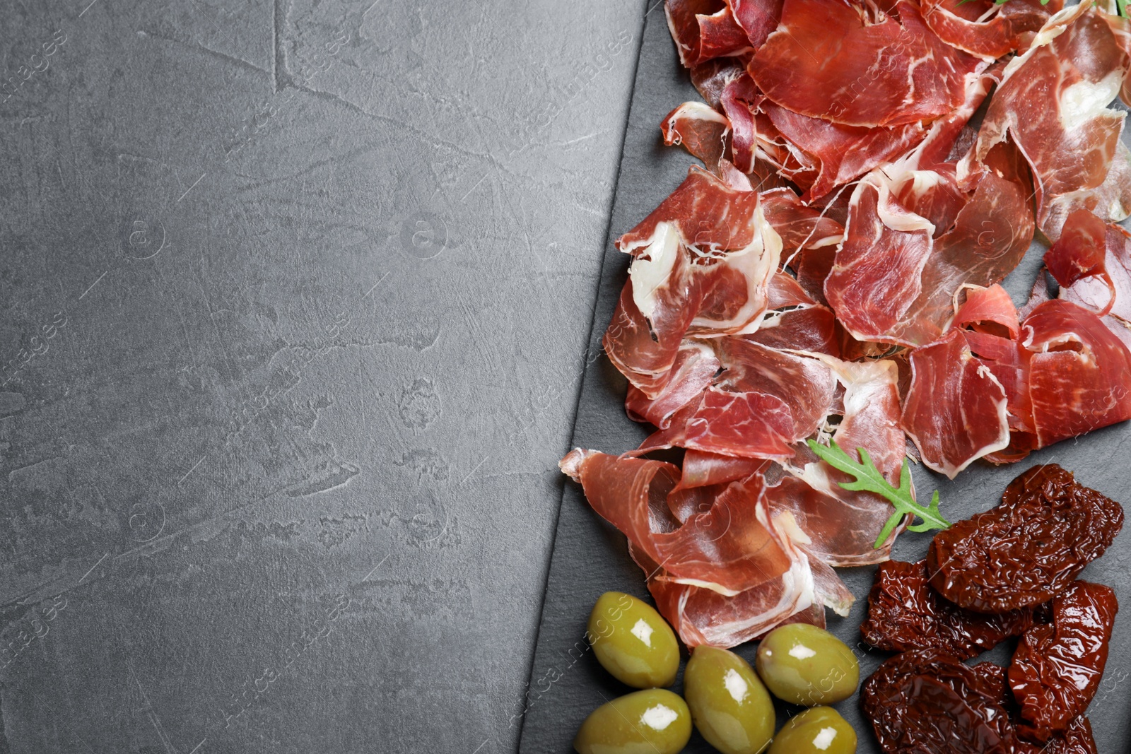 Photo of Tasty prosciutto served on grey table, top view. Space for text