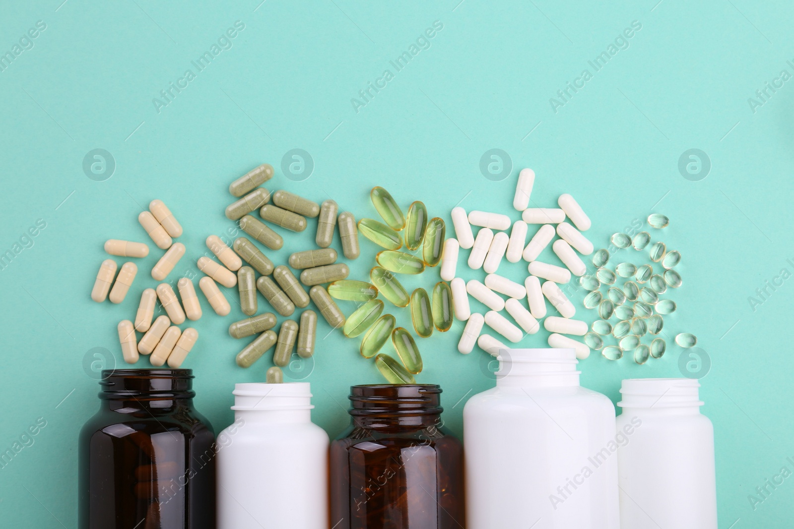 Photo of Bottles and different vitamin capsules on turquoise background, flat lay