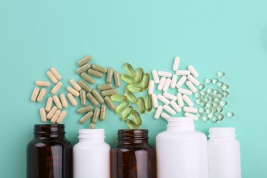 Photo of Bottles and different vitamin capsules on turquoise background, flat lay