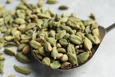 Photo of Spoon with dry cardamom pods on table, closeup