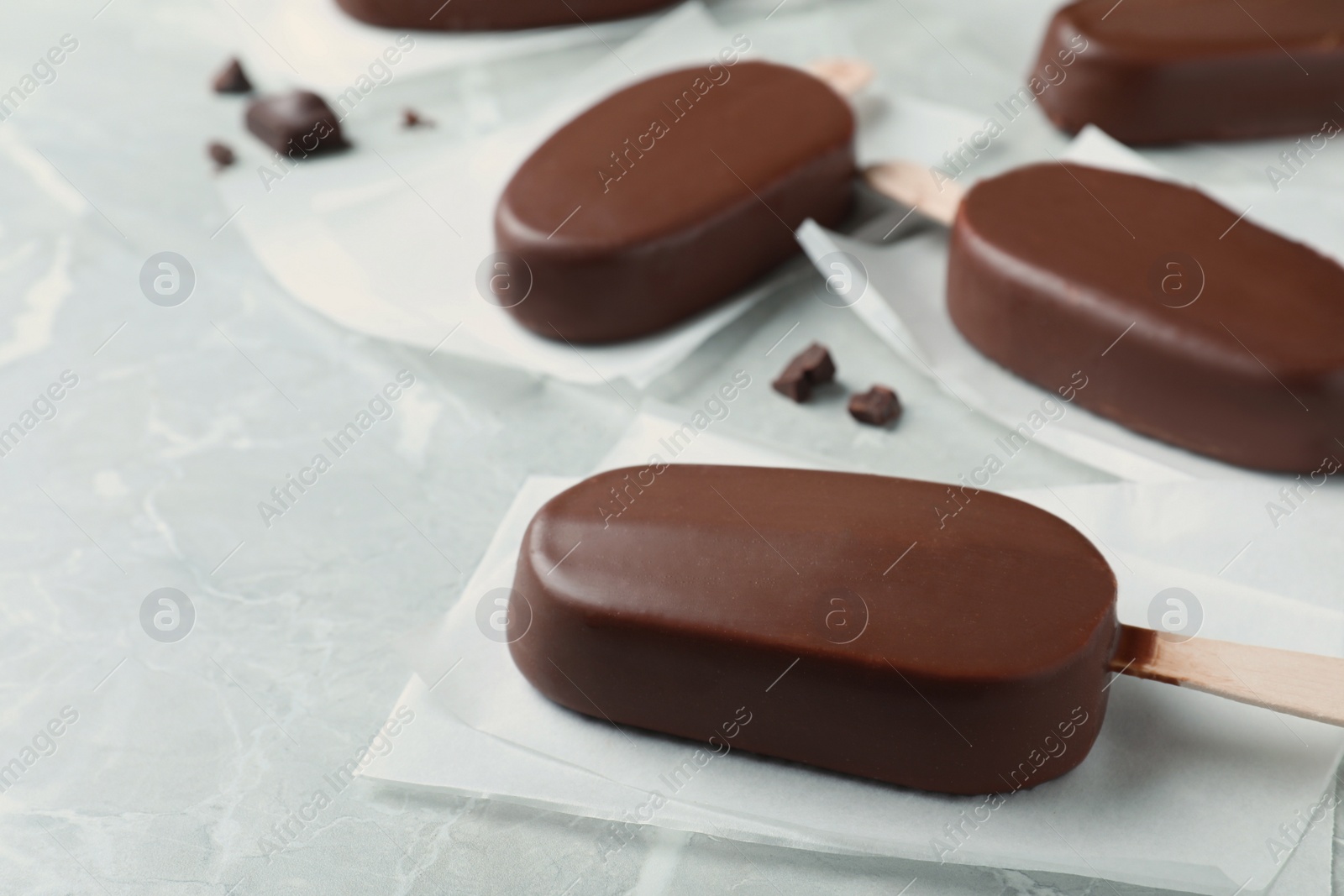 Photo of Glazed ice cream bars and chocolate chunks on light grey table, closeup