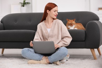 Photo of Woman working with laptop near cat on sofa at home