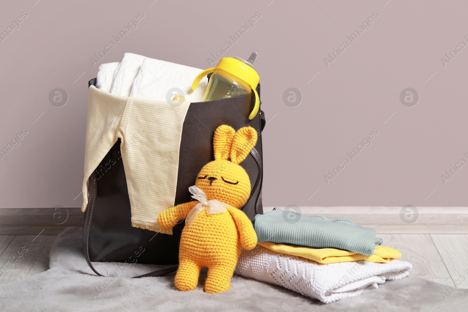 Photo of Mother's bag with baby's stuff on floor indoors. Space for text