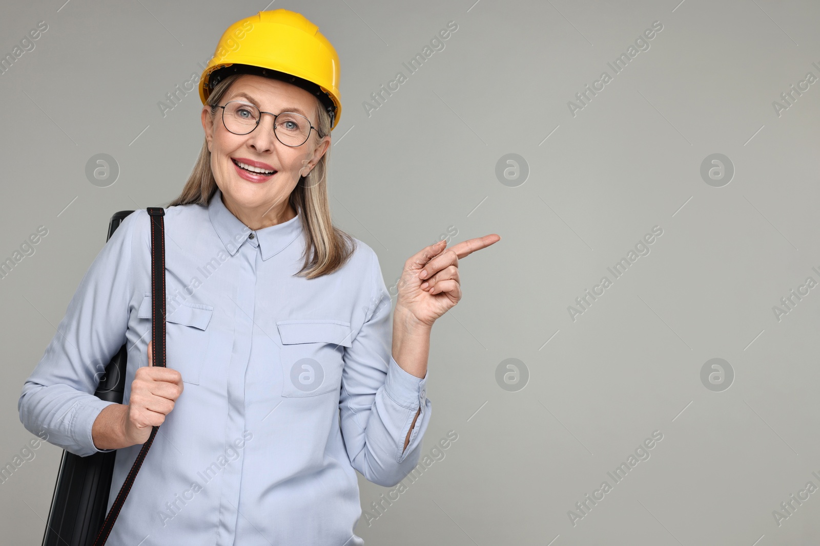 Photo of Architect in hard hat with tube pointing at something on grey background, space for text
