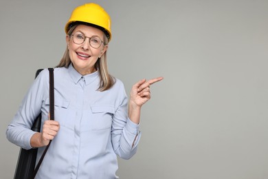 Architect in hard hat with tube pointing at something on grey background, space for text