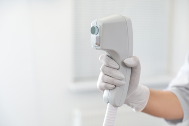 Photo of Young woman holding professional laser epilator in beauty salon, closeup. Space for text