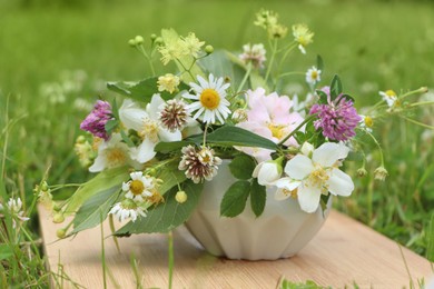 Ceramic mortar with different wildflowers and herbs on wooden board in meadow