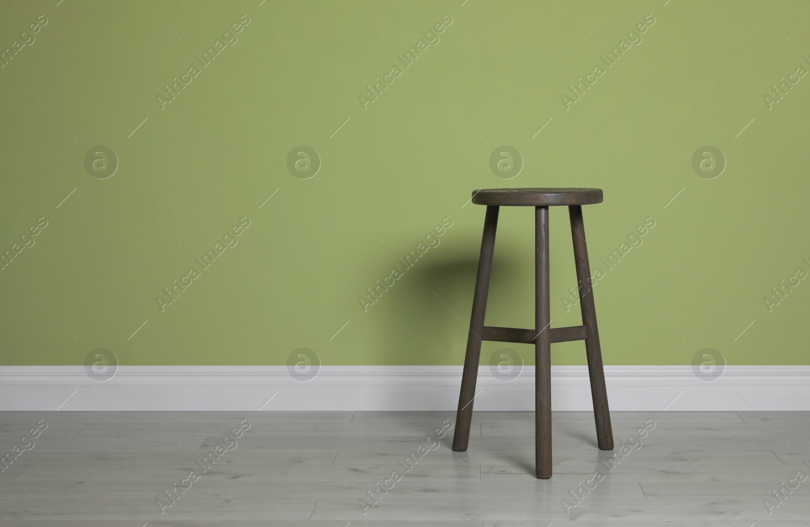 Photo of Stylish wooden stool near light green wall indoors. Space for text