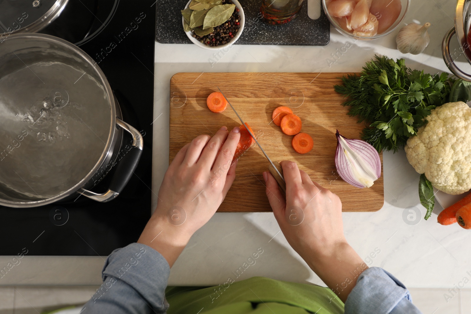 Photo of Woman cutting carrot to make bouillon at countertop, top view. Homemade recipe