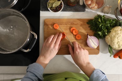 Photo of Woman cutting carrot to make bouillon at countertop, top view. Homemade recipe