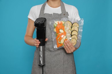 Photo of Woman holding sous vide cooker and vegetables in vacuum packs on light blue background, closeup