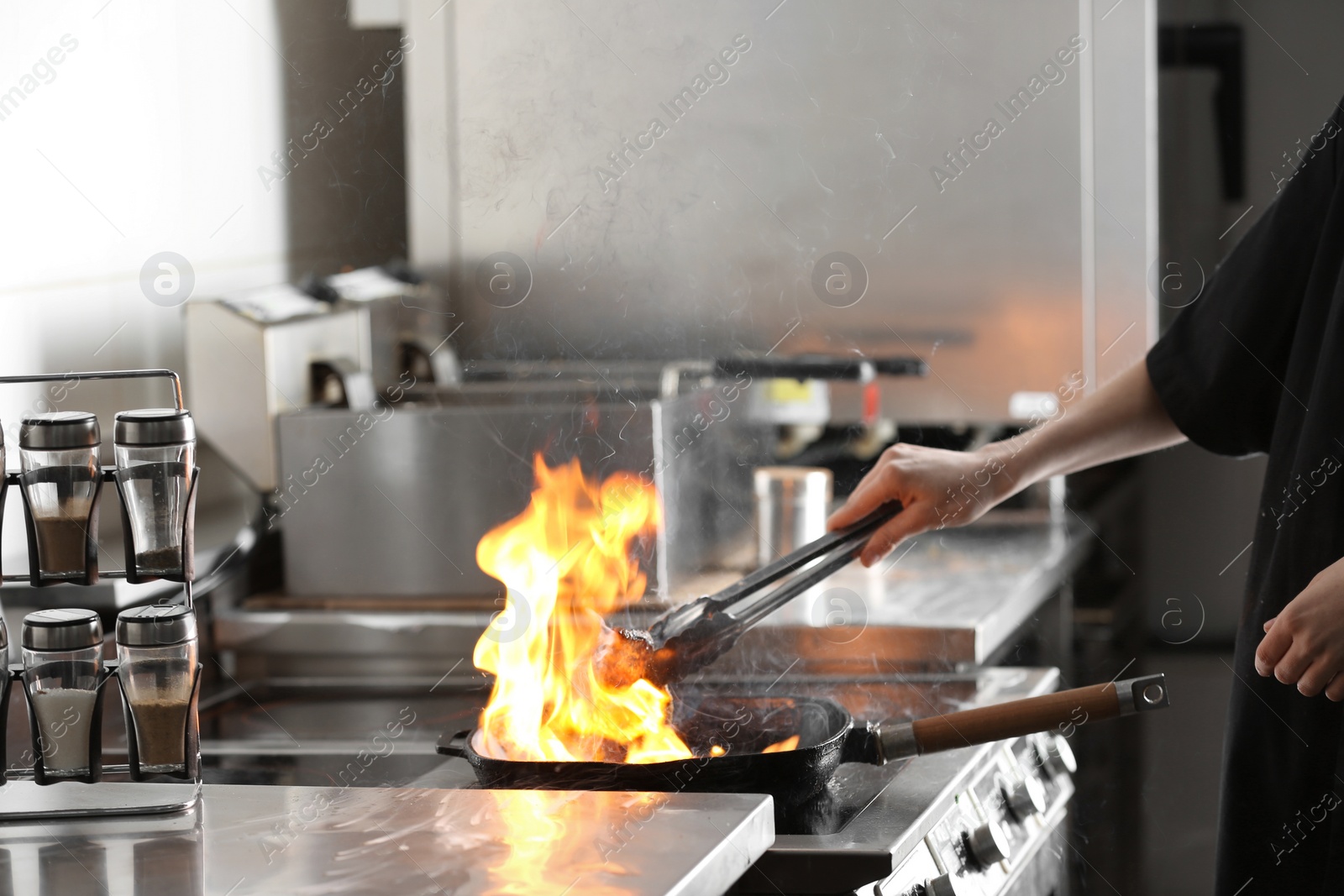 Photo of Female chef cooking meat with burning flame on stove in restaurant kitchen, closeup