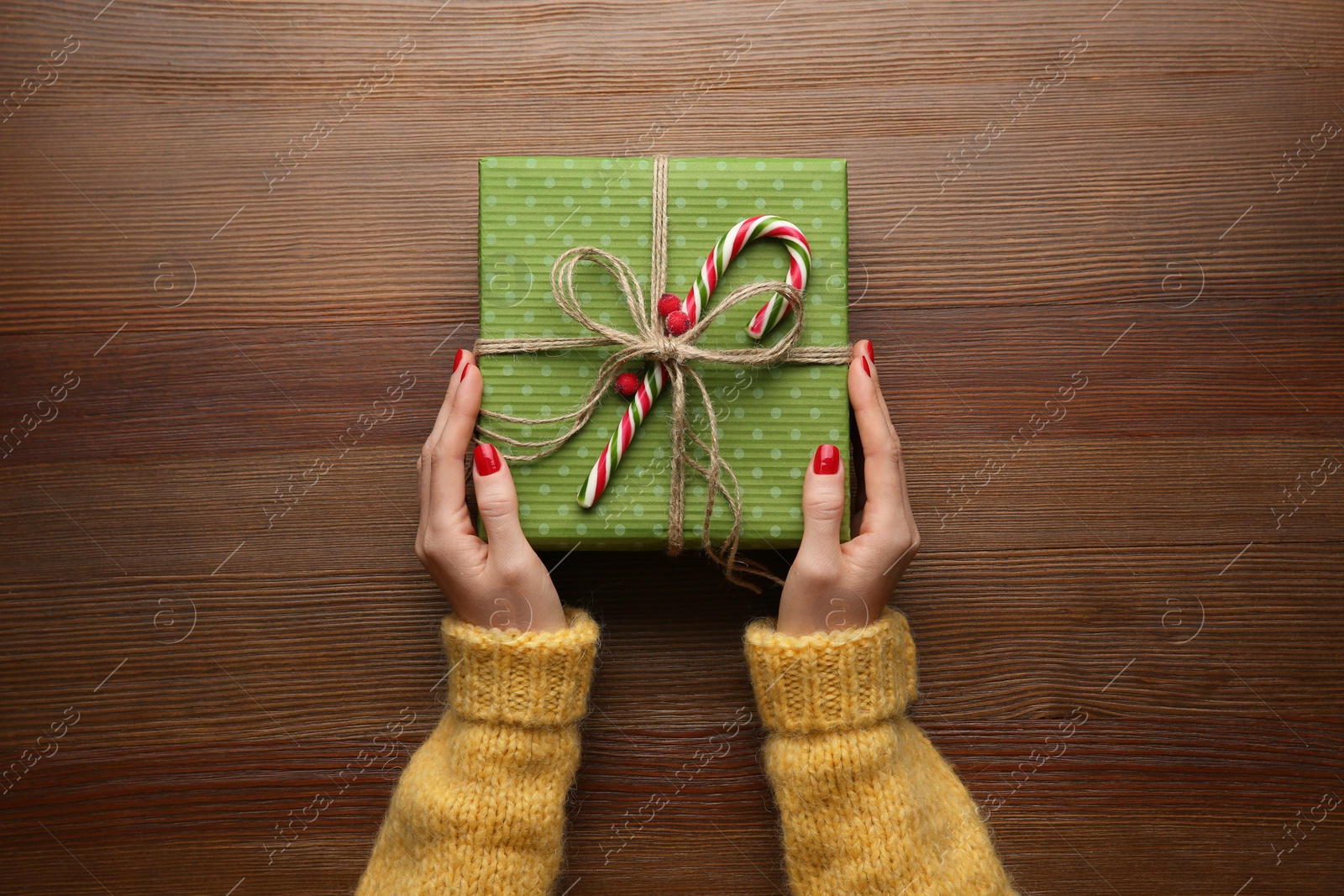 Photo of Woman holding green Christmas gift box at wooden table, top view