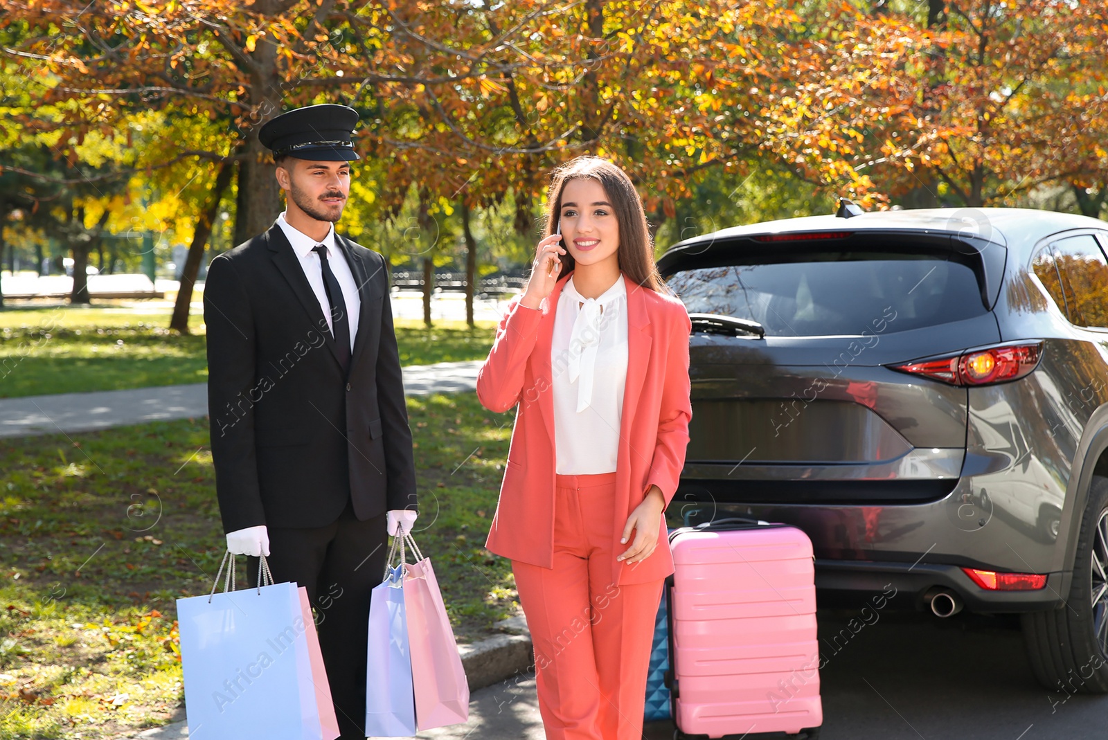 Photo of Handsome driver with shopping bags and young businesswoman near car outdoors