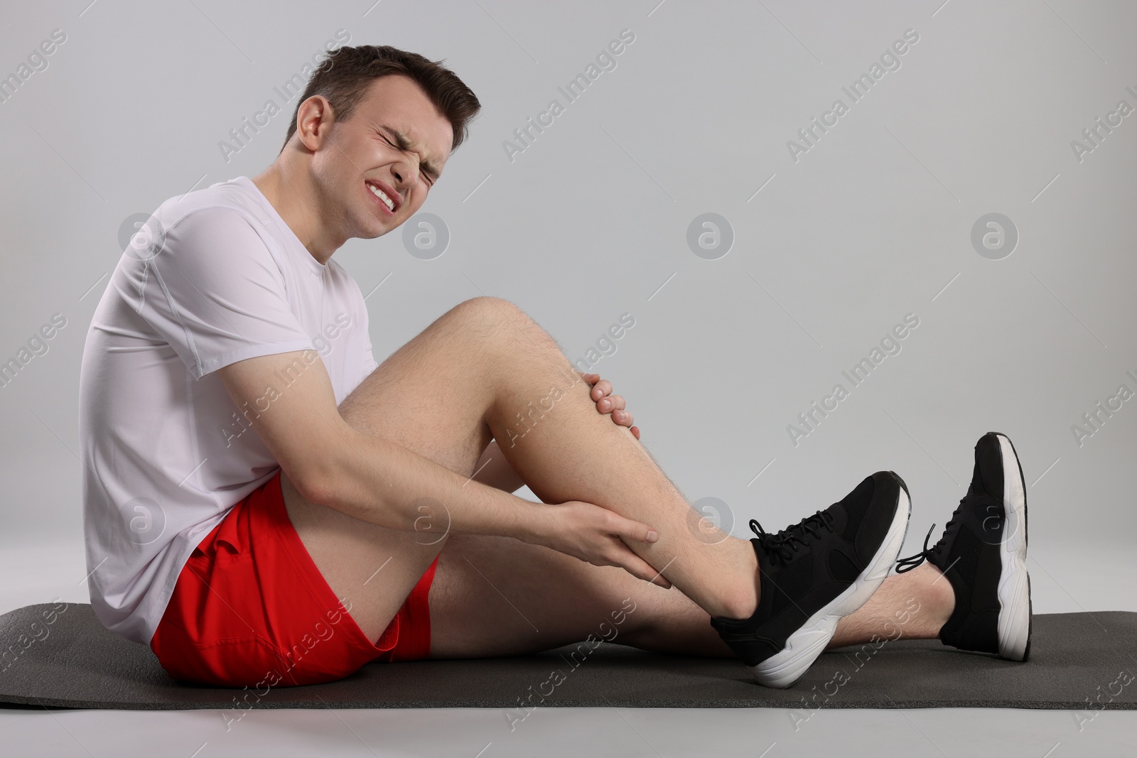 Photo of Man suffering from leg pain on mat against grey background