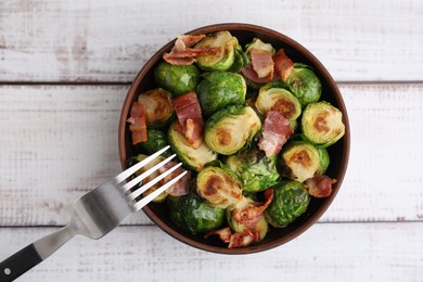 Photo of Delicious roasted Brussels sprouts and bacon in bowl on light wooden table, top view