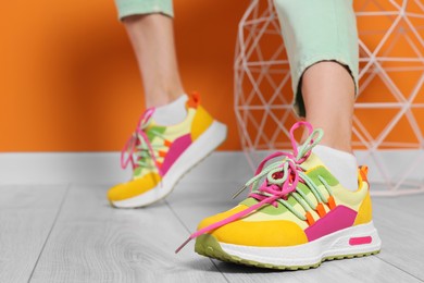 Woman wearing pair of new stylish sneakers near orange wall, closeup. Space for text