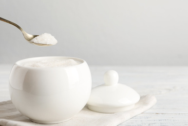 Photo of Taking spoon of white sugar from ceramic bowl on wooden table. Space for text