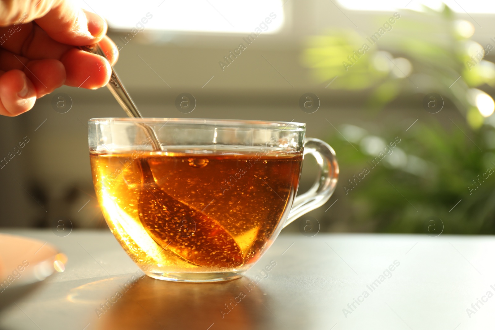 Photo of Woman stirring tea with spoon at table, closeup