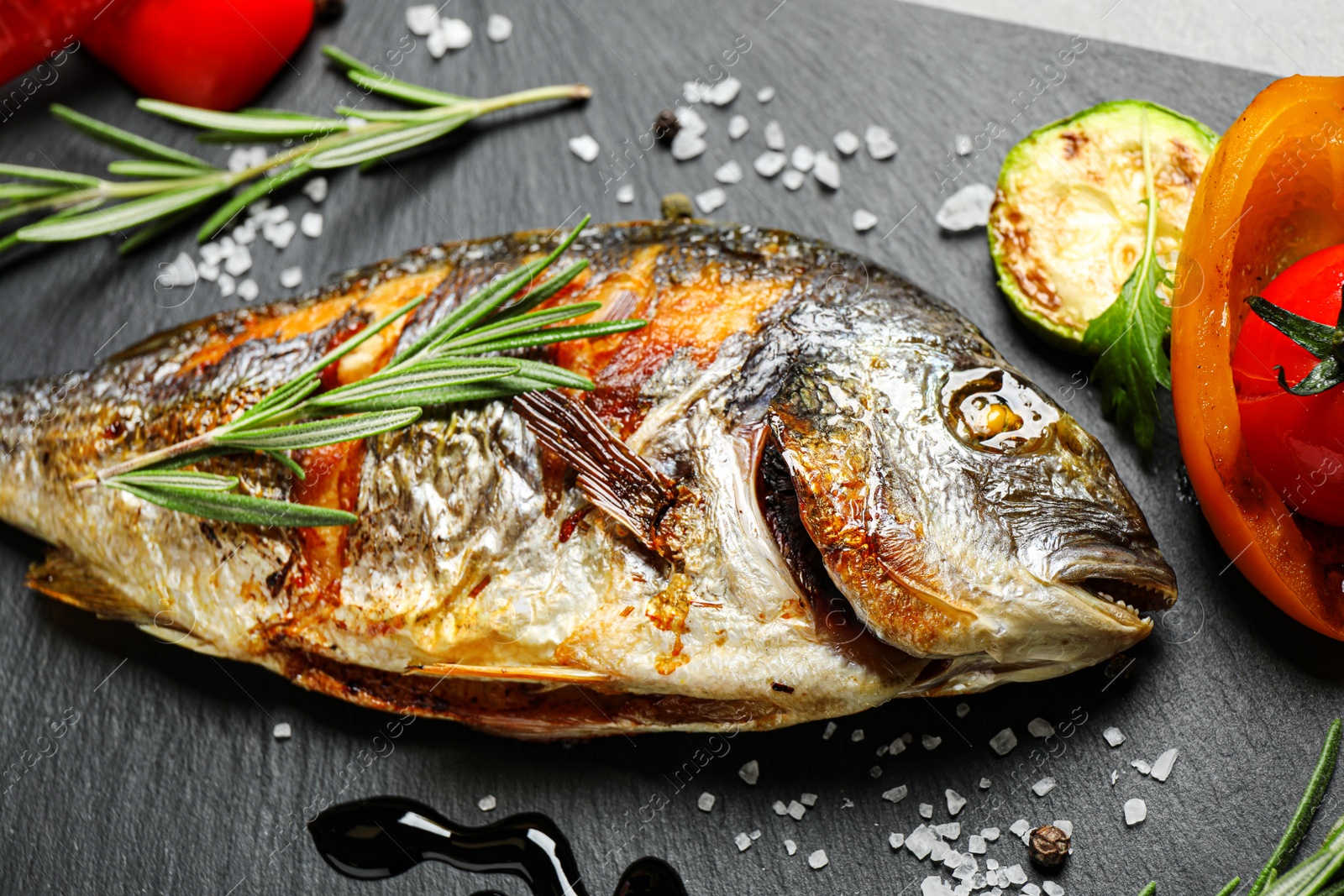 Photo of Delicious roasted fish and vegetables on black table, closeup