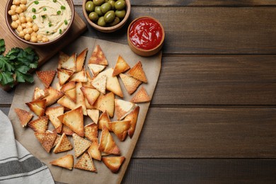 Photo of Delicious pita chips with hummus, olives and sauce on wooden table, flat lay. Space for text