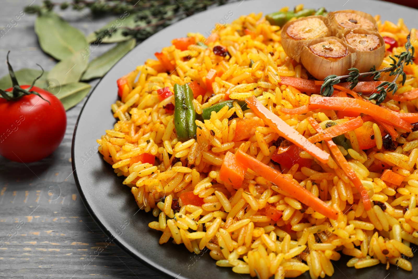 Photo of Tasty rice pilaf with vegetables on grey wooden table, closeup