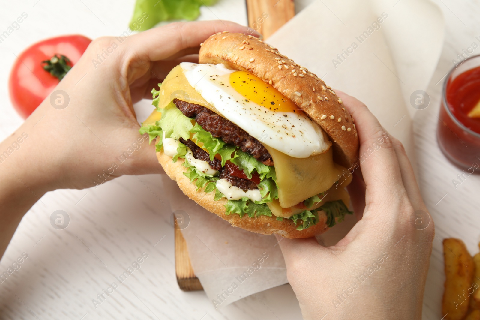 Photo of Woman holding tasty burger with fried egg over table, closeup