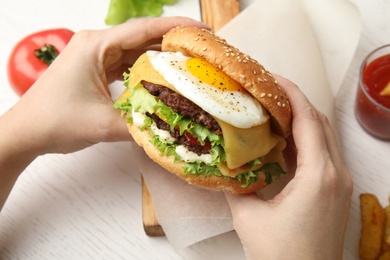 Woman holding tasty burger with fried egg over table, closeup