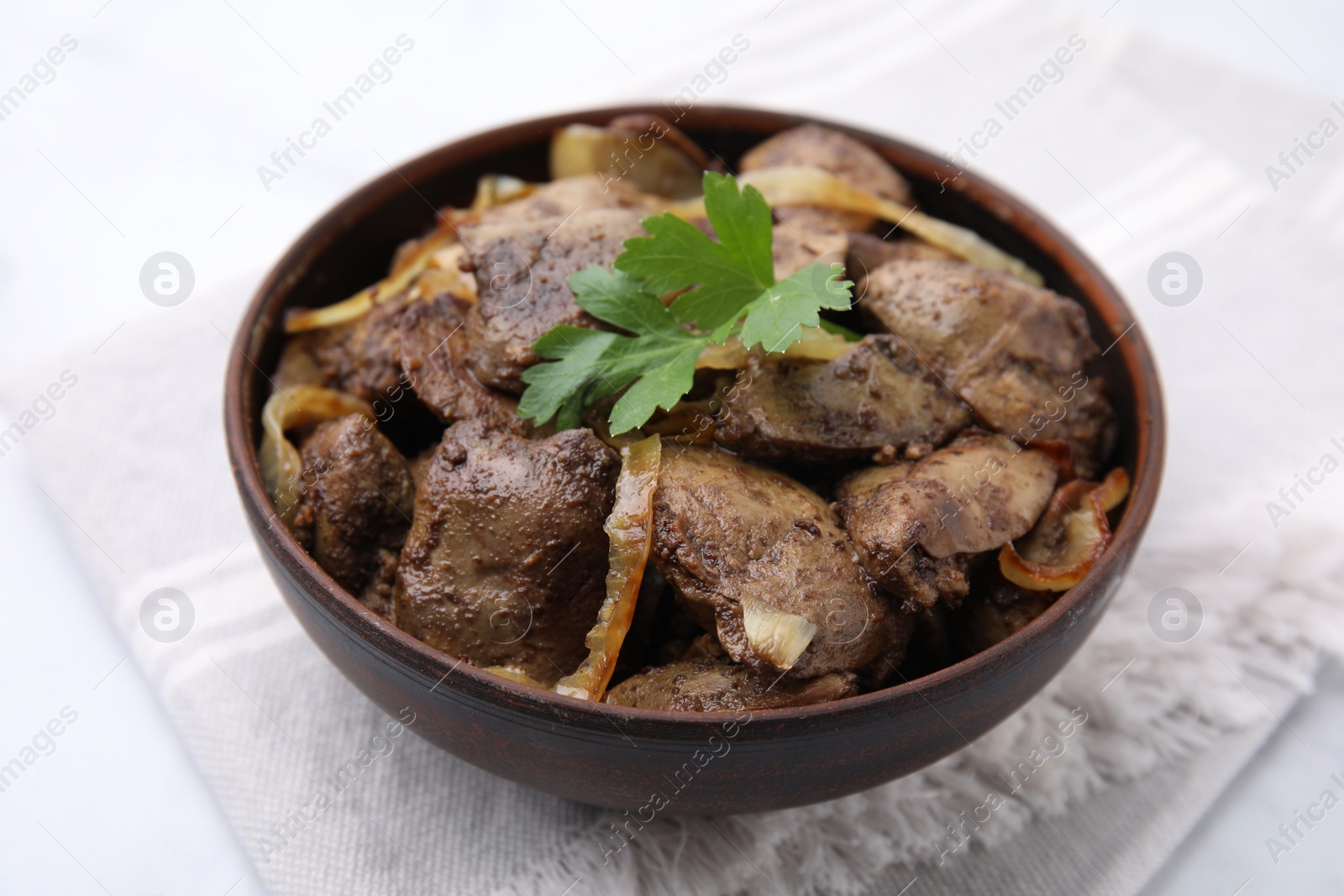 Photo of Tasty fried chicken liver with onion and parsley in bowl on white table, closeup