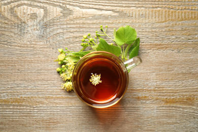 Photo of Cup of tea and linden blossom on wooden table, flat lay