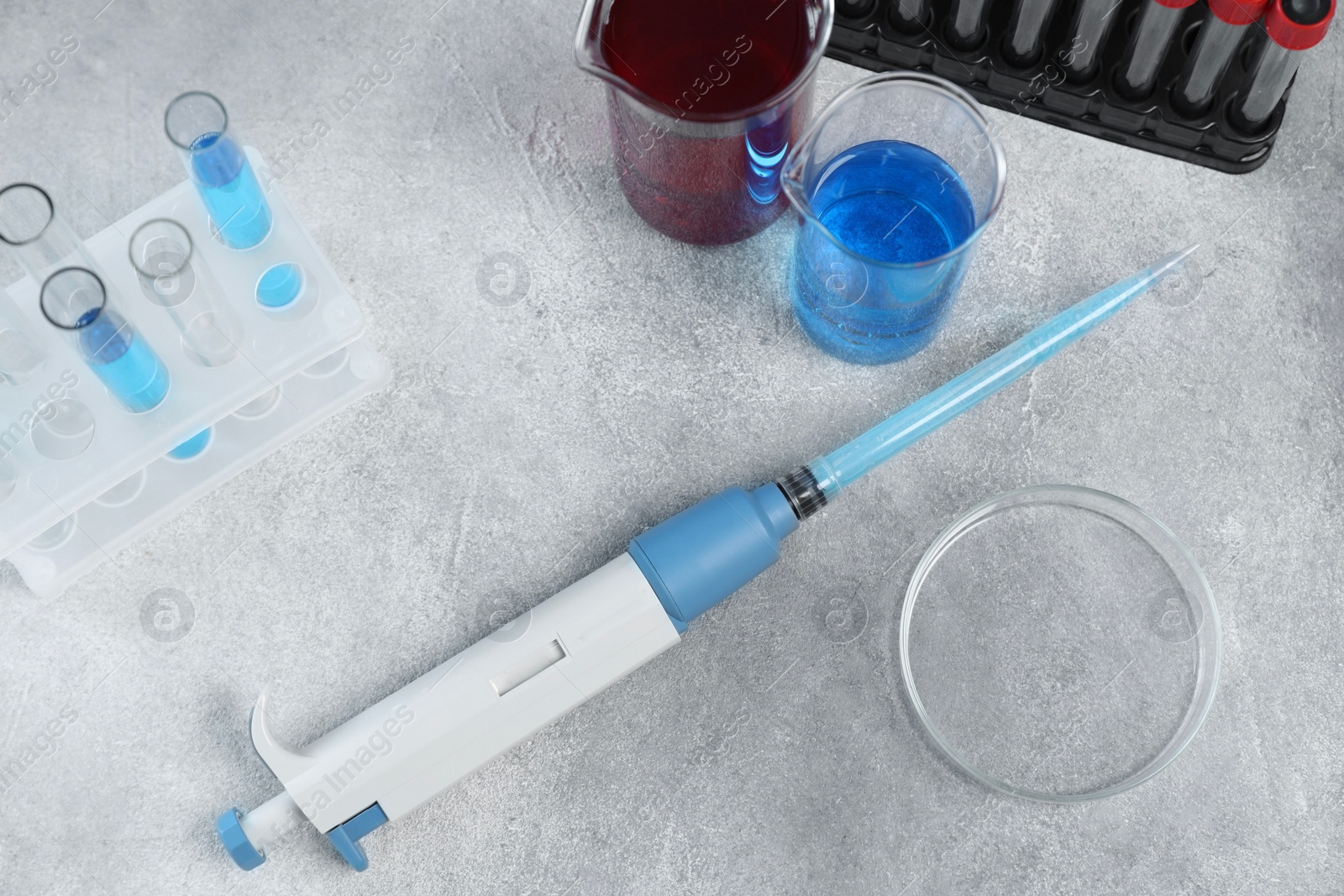 Photo of Laboratory analysis. Micropipette, petri dish, beakers and test tubes on light grey table, above view