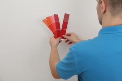 Photo of Man with palette choosing color for painting wall indoors, closeup. Interior design