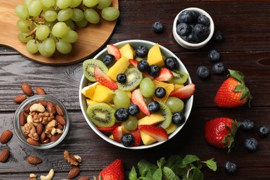 Photo of Tasty fruit salad in bowl and ingredients on wooden table, flat lay