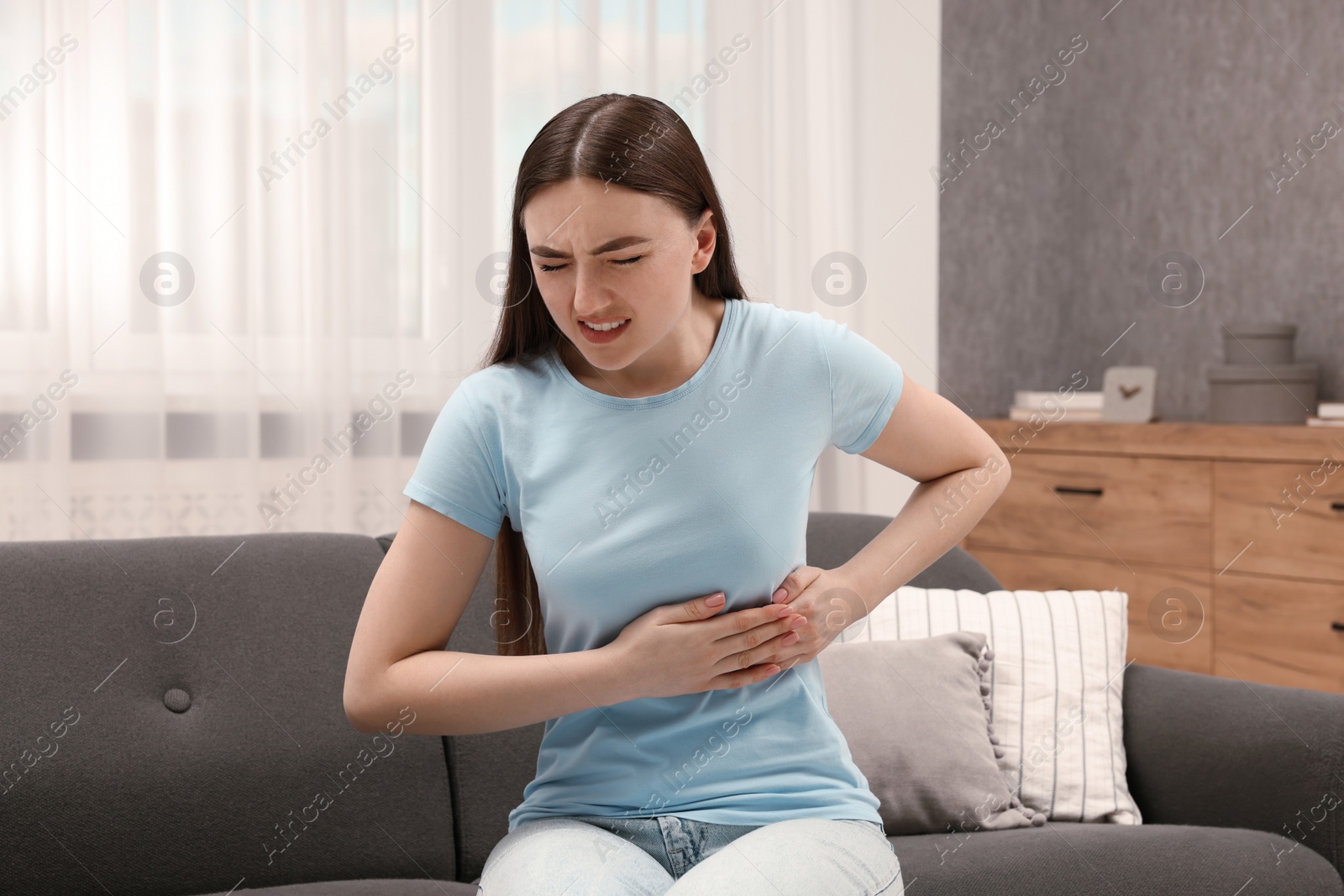Photo of Woman suffering from stomach pain on sofa indoors