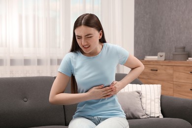 Photo of Woman suffering from stomach pain on sofa indoors