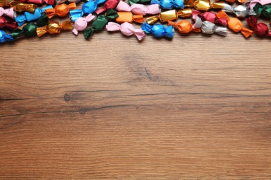 Photo of Many candies in colorful wrappers on wooden table, flat lay. Space for text