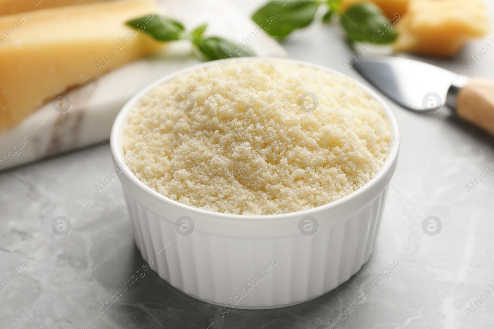 Photo of Bowl with grated parmesan cheese on light table, closeup