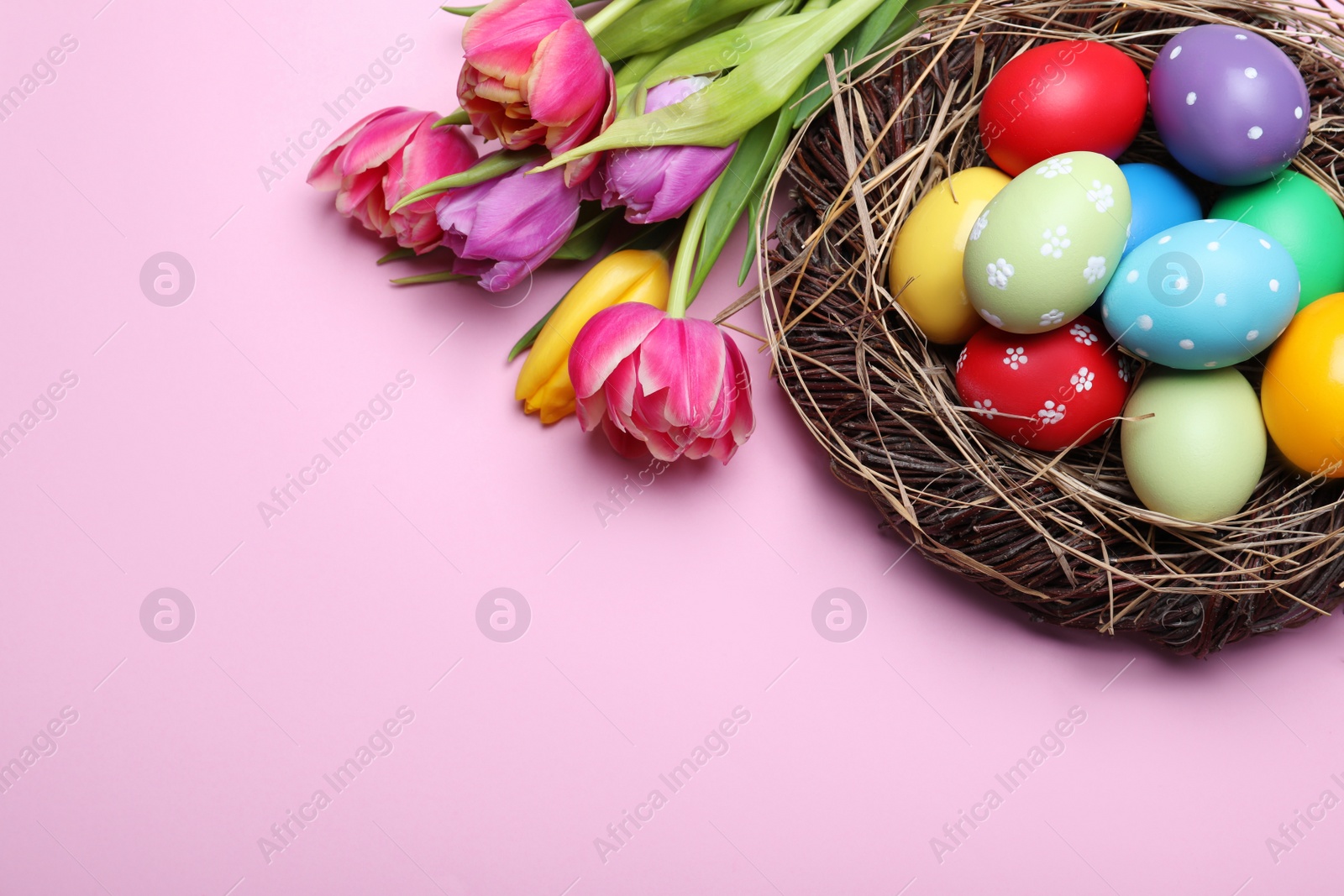 Photo of Bright painted eggs and spring tulips on pink background, flat lay with space for text. Happy Easter