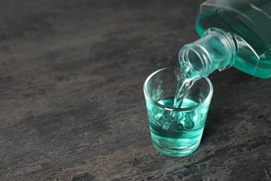 Photo of Pouring mouthwash in glass and space for text on dark background. Teeth care