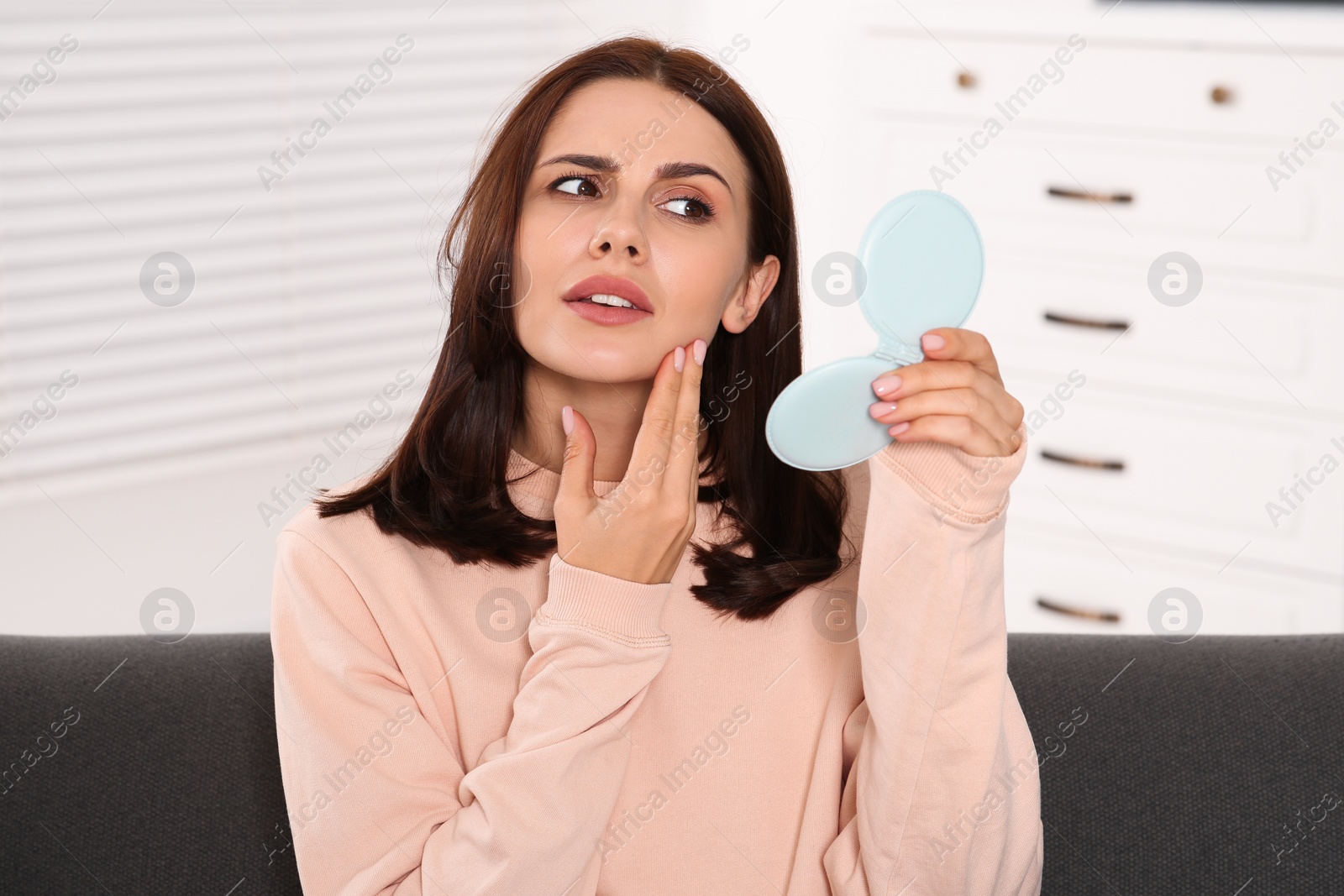 Photo of Young woman looking in mirror and touching her face indoors. Hormonal disorders