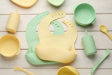 Photo of Flat lay composition with silicone baby bibs and plastic dishware on white wooden background