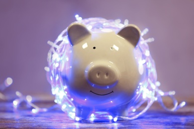 Cute piggy bank with Christmas lights on table