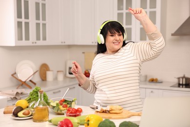Happy overweight woman with headphones dancing while cooking in kitchen