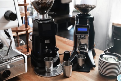 Photo of Modern coffee grinding machines with metal cups and saucers on wooden bar counter