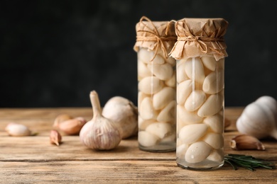 Photo of Preserved garlic in glass jars on wooden table against dark background. Space for text