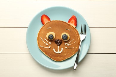 Photo of Creative serving for kids. Plate with cute cat made of pancakes, berries, cream, banana and chocolate paste on white wooden table, top view