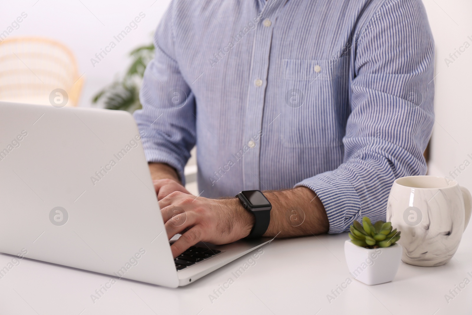 Photo of Young man with smart watch working on laptop at table in office, closeup