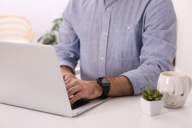 Photo of Young man with smart watch working on laptop at table in office, closeup