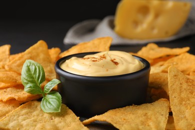 Delicious nachos and cheese sauce with basil on table, closeup